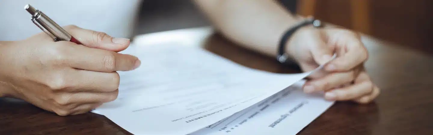 A person holding a pen and a document while reviewing or signing it, sitting at a table.