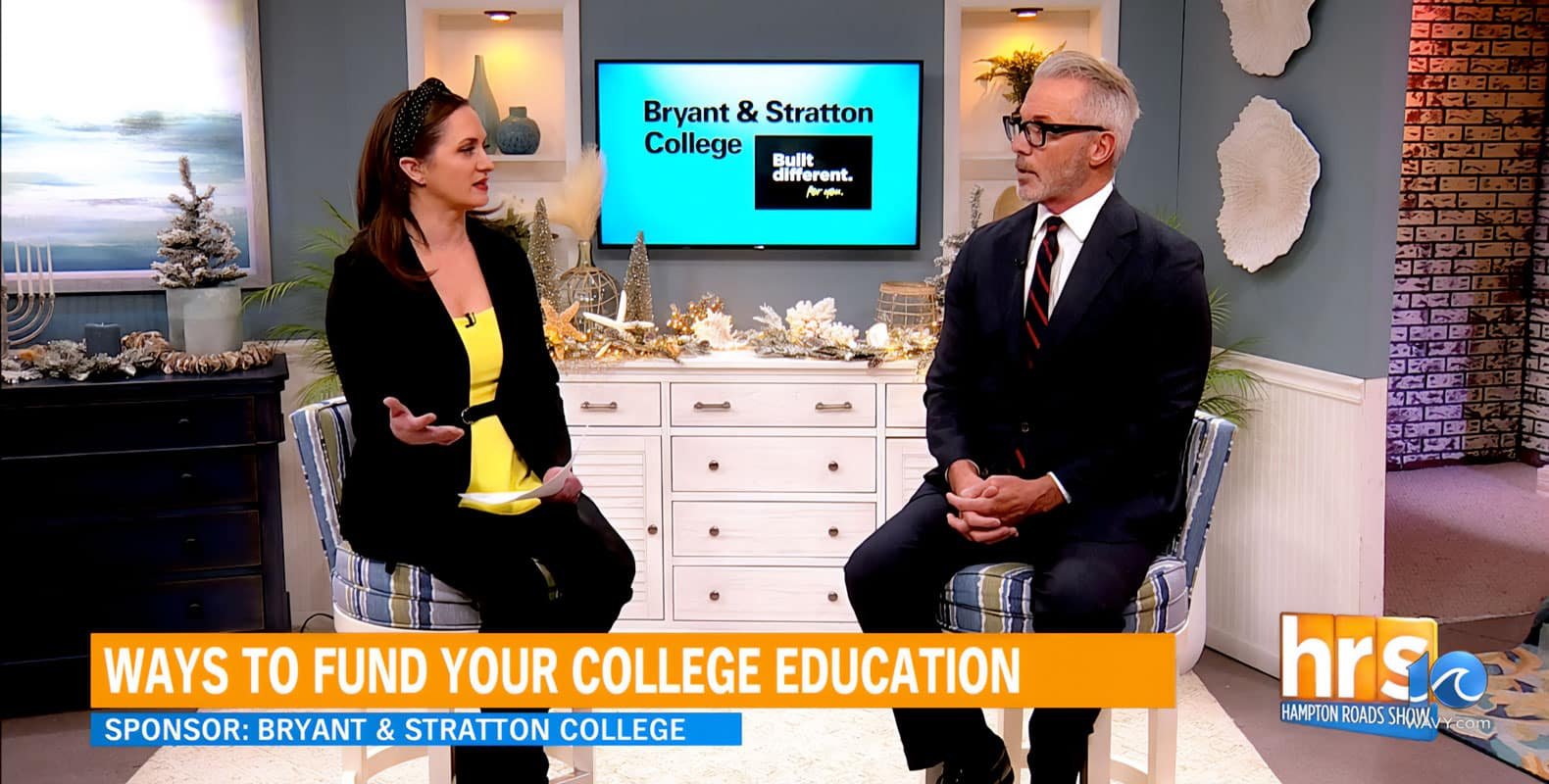 Two people sitting in a studio discussing ways to fund college education, with a Bryant & Stratton College sign in the background.
