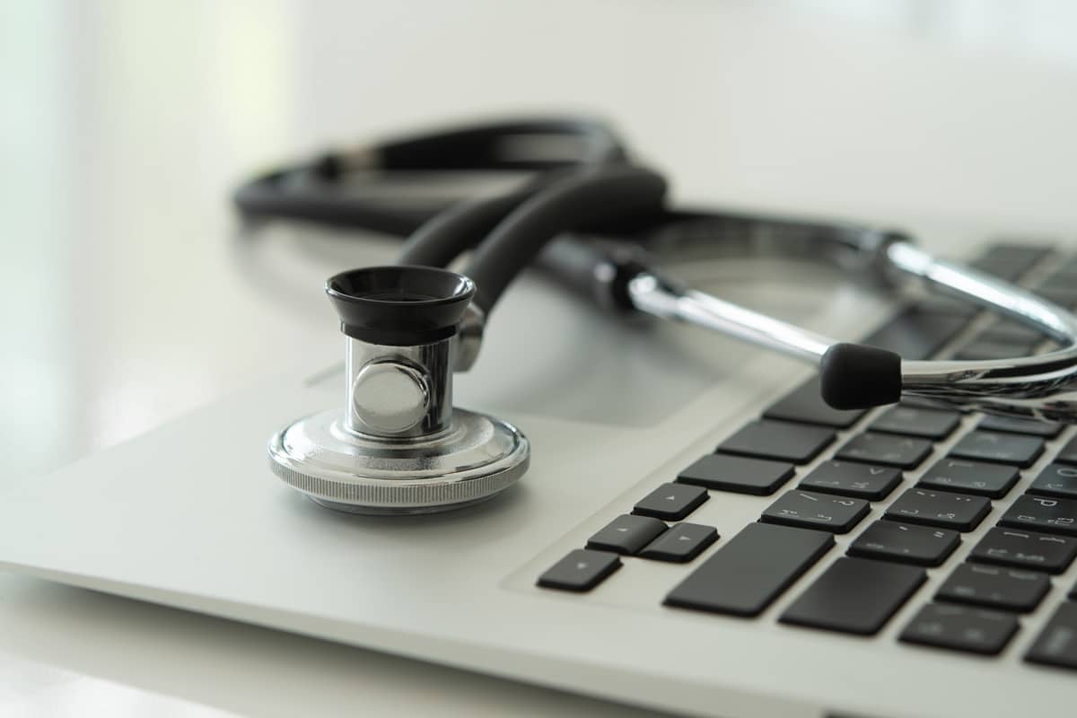 A stethoscope lying on top of a silver laptop keyboard.