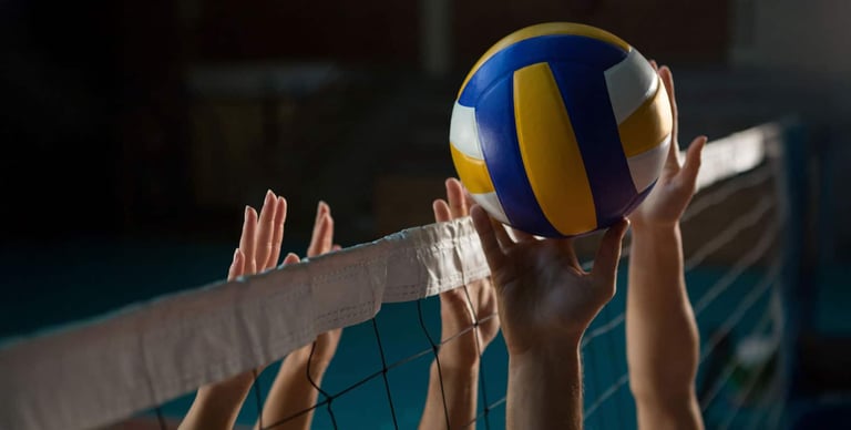 A volleyball in mid-air as multiple hands reach for it over the net during a game.