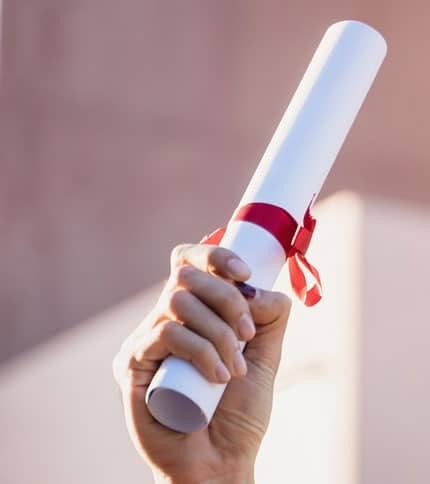A hand holds up a rolled-up certificate tied with a red ribbon against a blurred background.