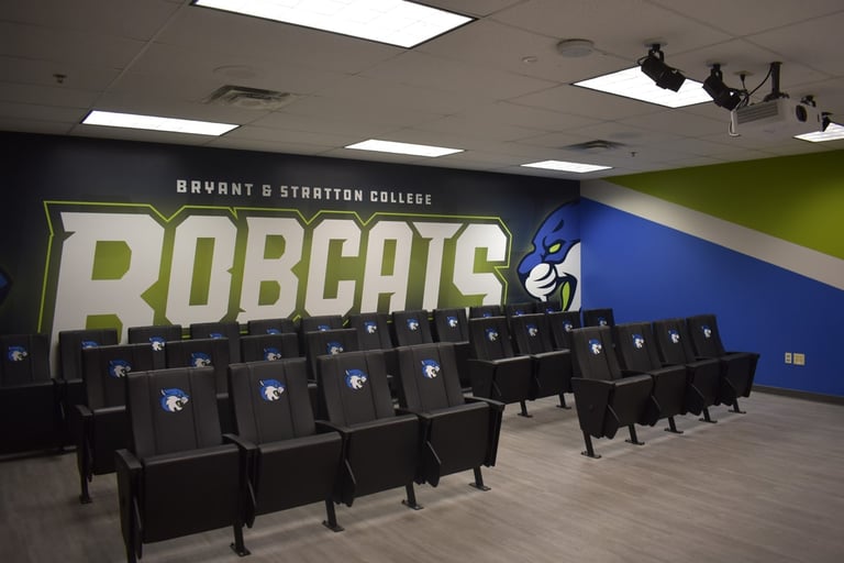 A college room with several rows of black chairs and "Bryant & Stratton College Bobcats" logo on the wall.