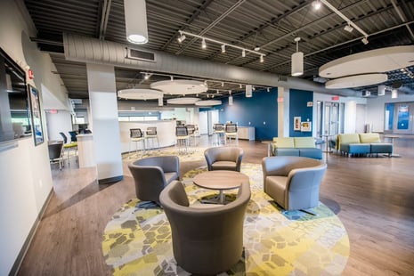 Modern open lounge area with round chairs, sofas, and a central table on a patterned rug, with bar stools in the background.