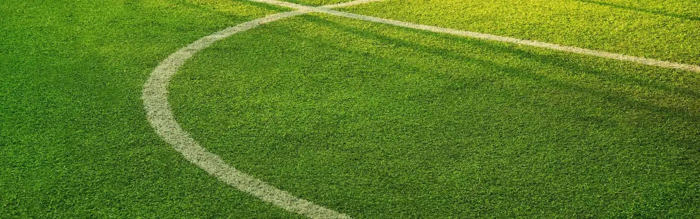 Close-up of the corner section of a football field, with white lines marking the boundary and green grass.