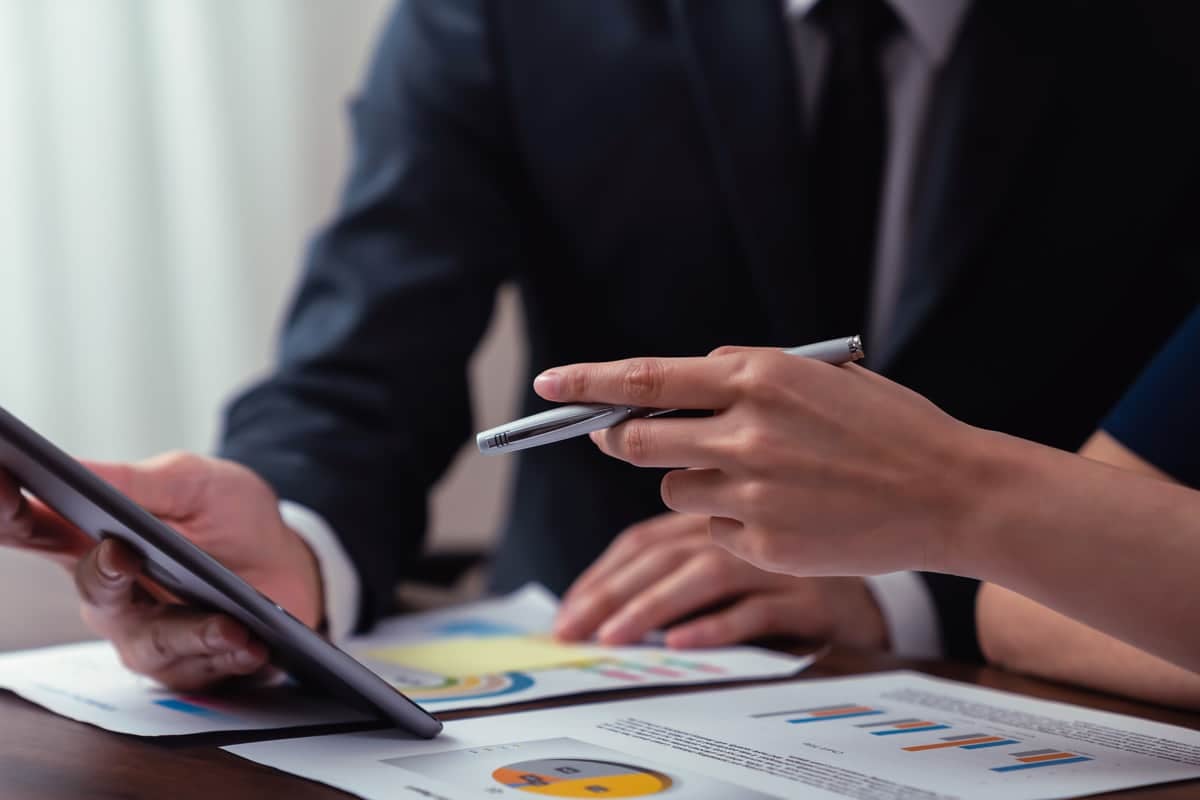 Close-up of two people in suits reviewing data on a tablet with charts and graphs on the table.