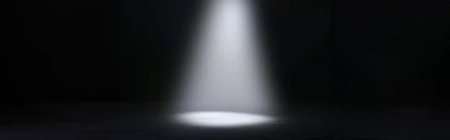 A single spotlight shines down on a dark, empty stage or room.