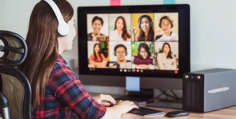 Woman wearing headphones participating in a video conference on a computer with eight people on the screen.