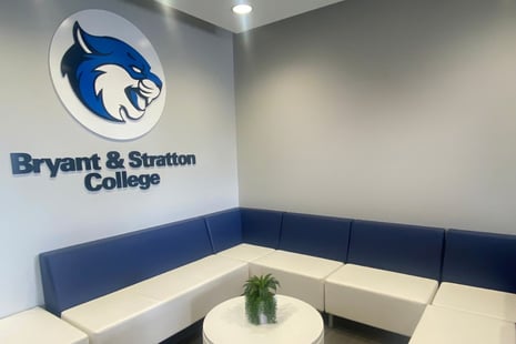 Reception area of Bryant & Stratton College with blue and white seating and a logo of a mascot on the wall.