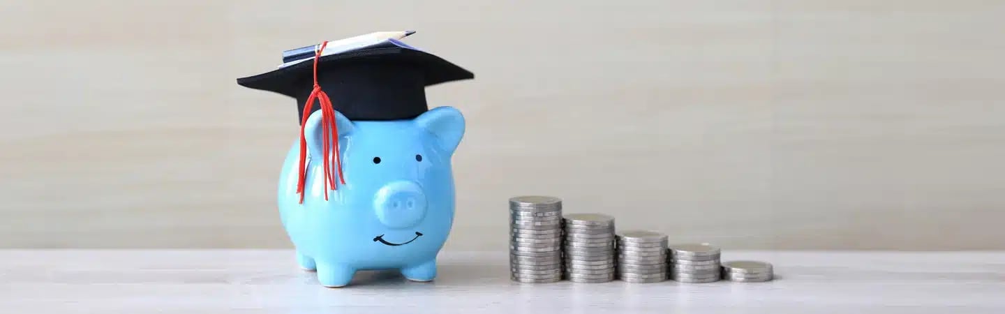 A blue piggy bank with a graduation cap next to a row of stacked coins symbolizing education savings.