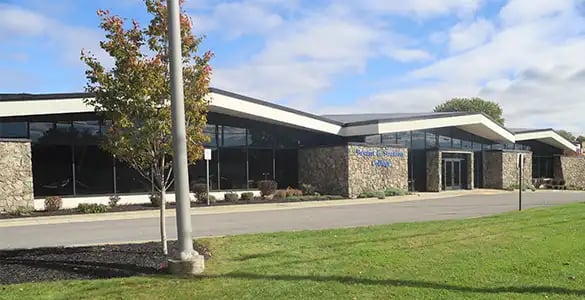 A modern building with a stone facade, large windows, and an angled roof set against a partly cloudy sky.