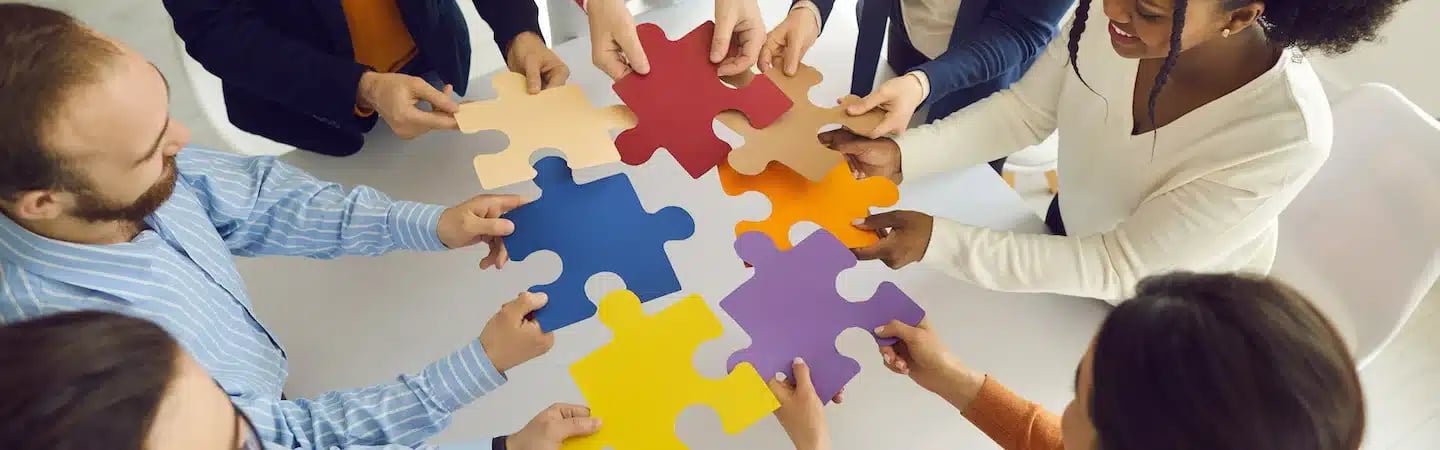 A diverse group of people collaborate, holding colorful puzzle pieces together in a completed formation.