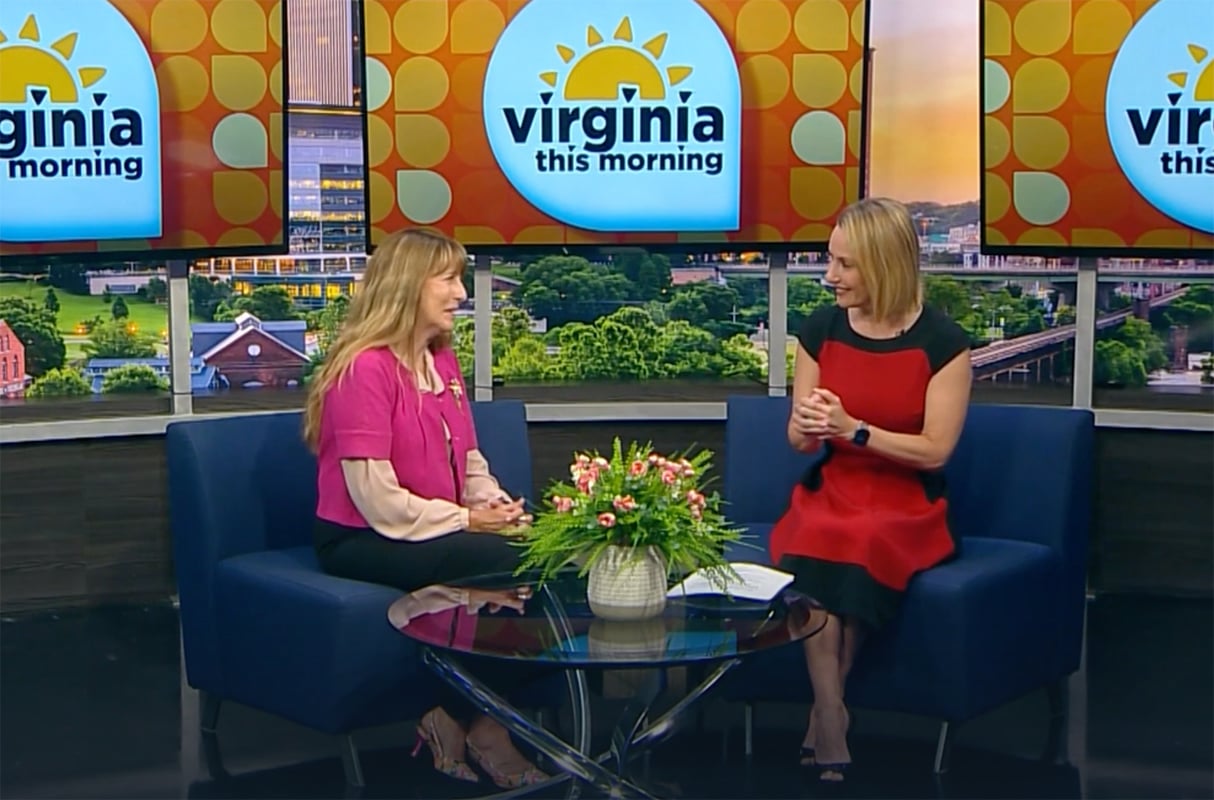 Two women sit and talk on the “Virginia This Morning” TV set, discussing Bryant & Stratton College’s Business programs. A small flower arrangement sits on the glass table between them as they share smiles during their conversation.