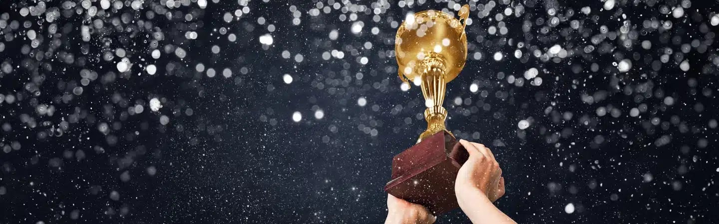Hands holding up a golden trophy with a dark, glittering background.