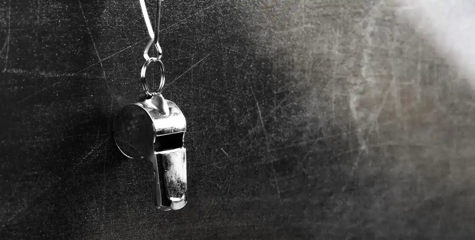 A metal whistle hanging by a string against a dark, textured background.