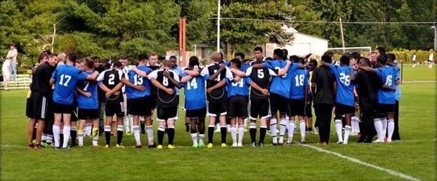 A soccer team in blue jerseys huddles together with arms around each other on the field before the game.
