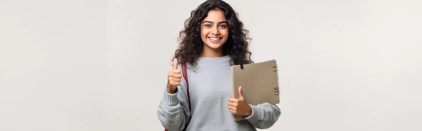 Person smiling and giving a thumbs-up, holding a notebook and bag, wearing a light gray sweater, standing against a plain background.