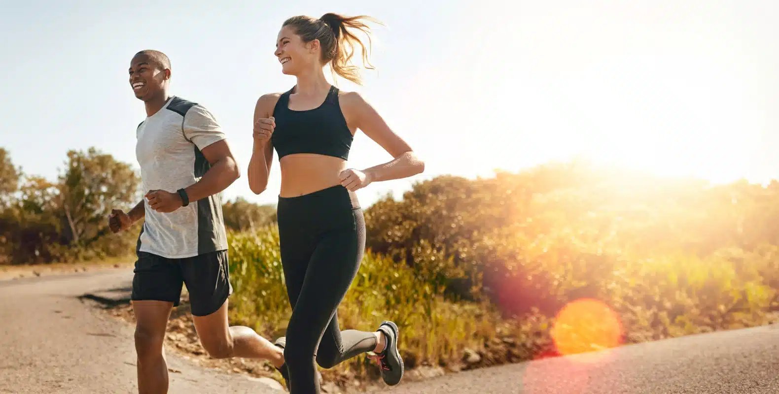A man and a woman jogging together on a sunny day, with trees and bushes in the background.