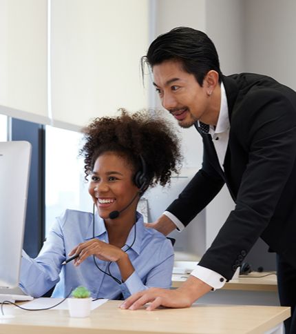 A Sales Supervisor and a colleague in a suit are looking at a computer.