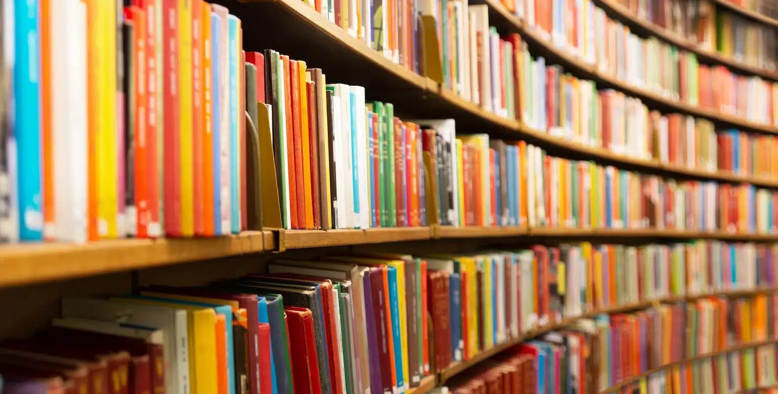 A curved bookshelf filled with colorful books arranged neatly in a library.