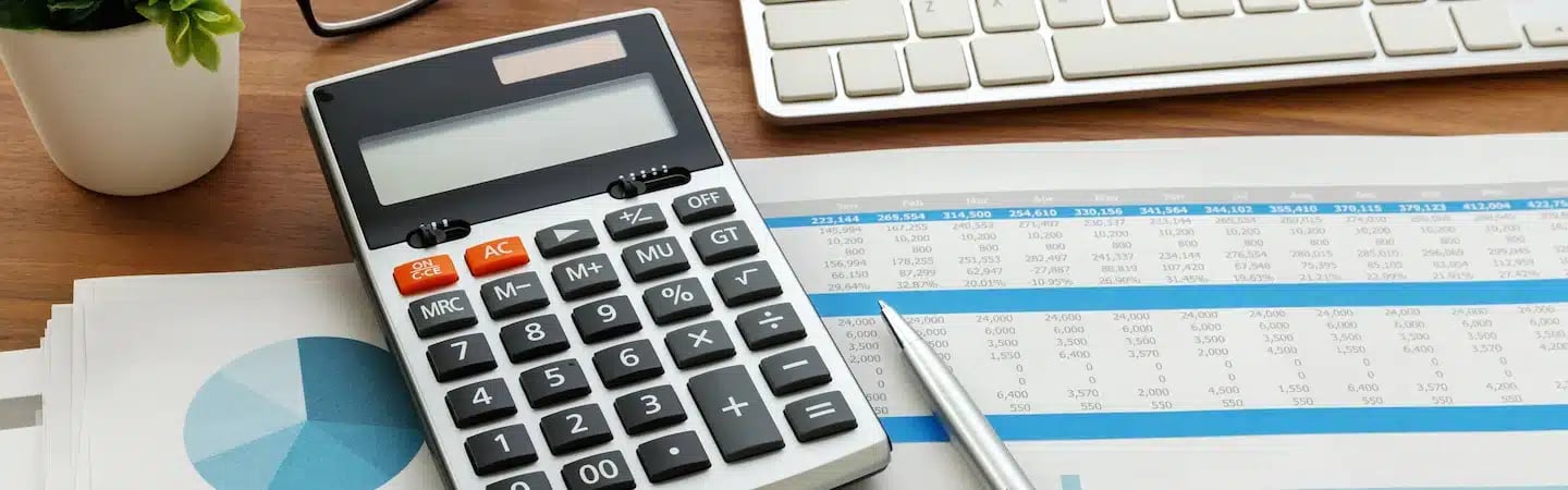 Calculator, pen, and financial documents on a desk with a keyboard in the background.