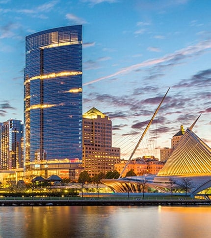 A vibrant skyline of Milwaukee at dusk, featuring modern buildings and the illuminated Milwaukee Art Museum by the waterfront.