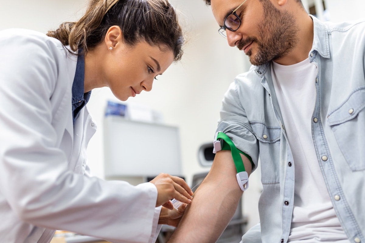 A healthcare professional prepares to draw blood from a patient's arm in a clinical setting.
