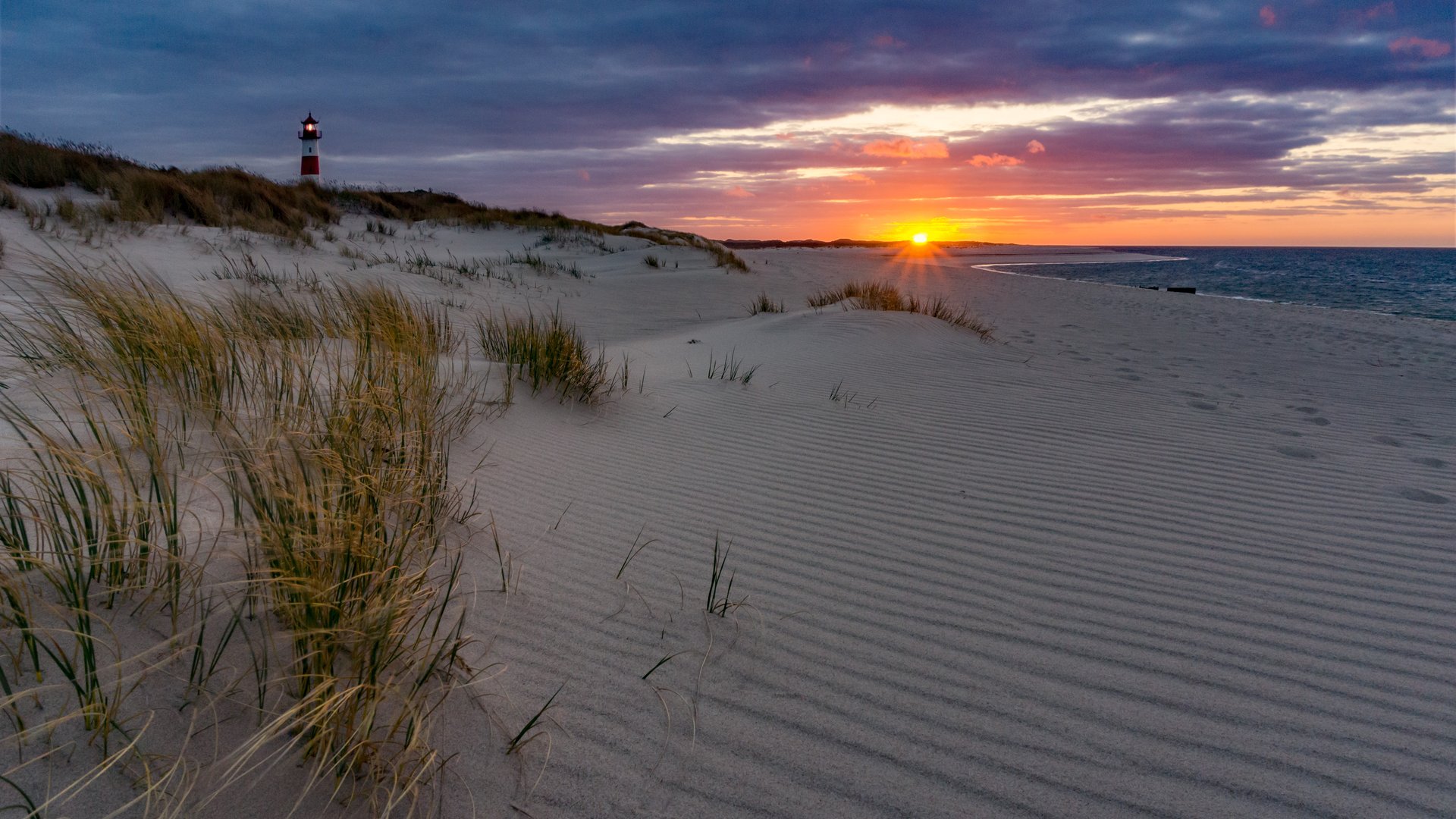 Ellenbogen Kiteboarding Sylt with white dune and lighthouse with sunset and sea in the background