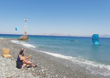 Psalidi Beach Kiteboarding in Kos instructor with a student sitting on the stony shore with a kite laying on the water