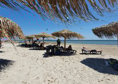Keros beach Kitesurfing in Limnos Greece pleople laying in their beach chairs on thite sand and three kites flying on the sea in the background on a great sunny windy day