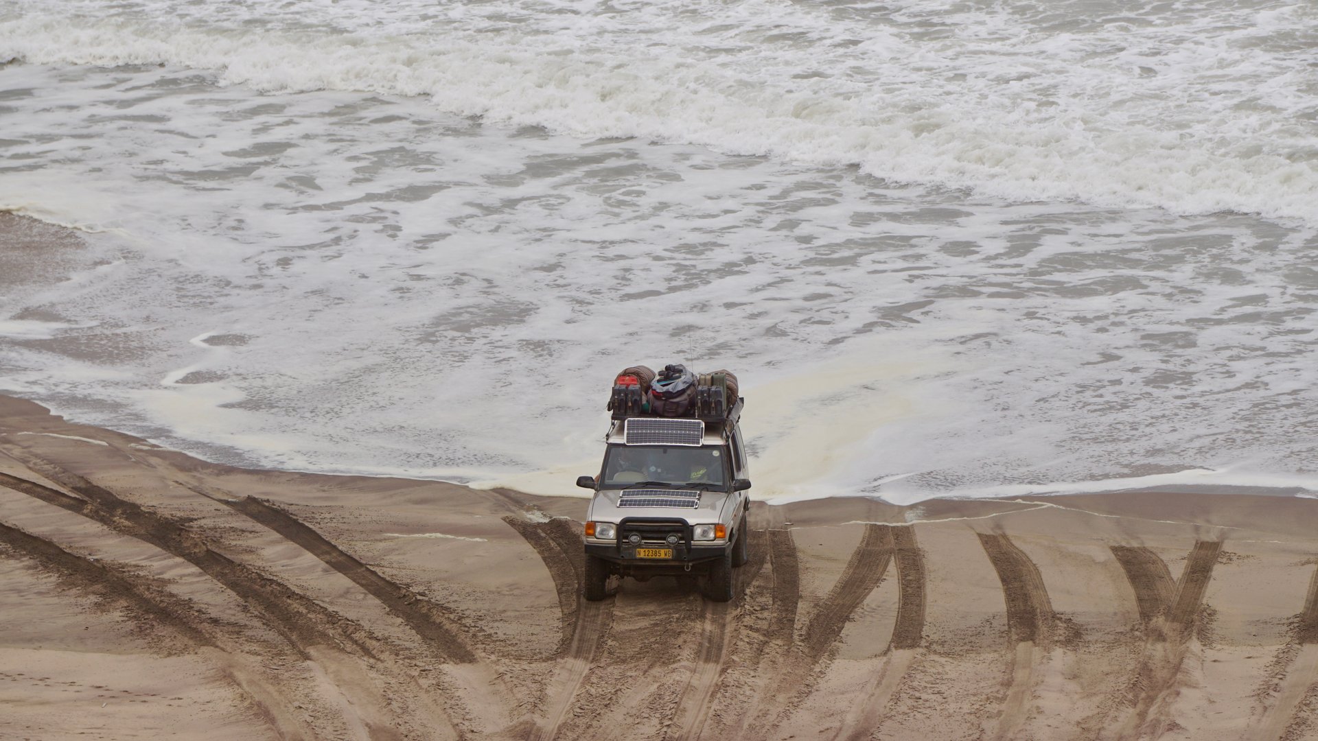 Fully packed Jeep riding away from incoming wave in Namibia