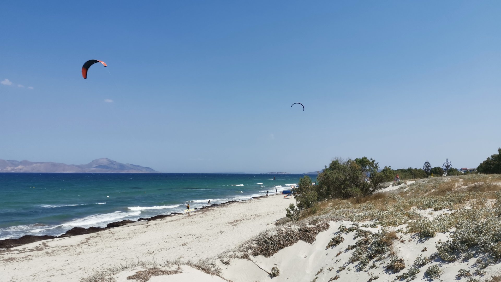 Mastichari Beach Kitesurfing in Kos natural hilly beach with fine wihte sand and 2 kitesurfers in the background on the windy sea