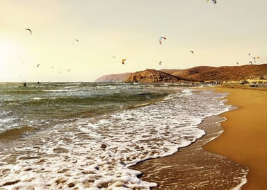 Prasonisi Beach Kiteboarding in Greeece image with about 20 kites in the yellow sunset and brownish sand in front