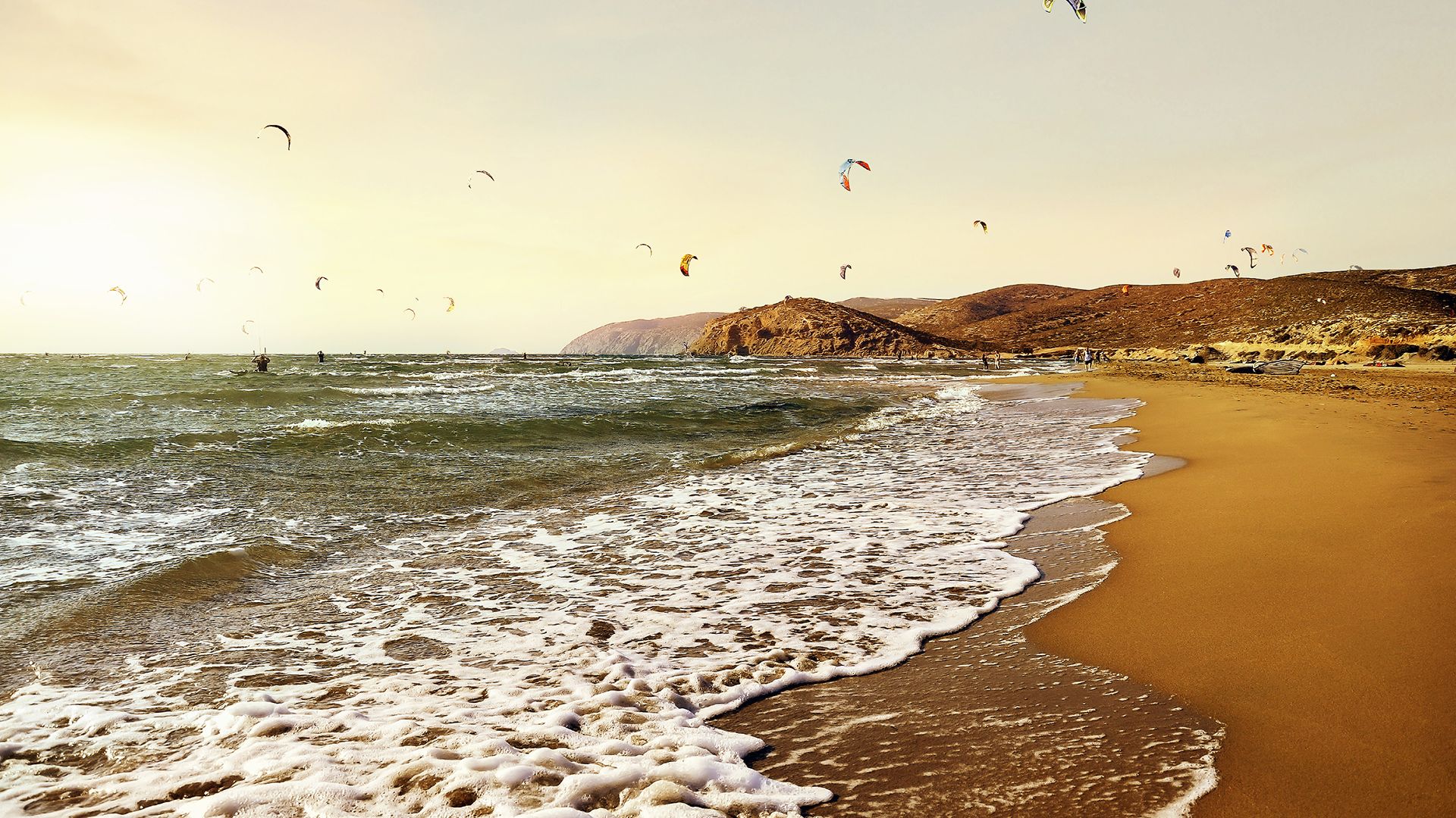 Prasonisi Beach Kiteboarding in Greeece image with about 20 kites in the yellow sunset and brownish sand in front