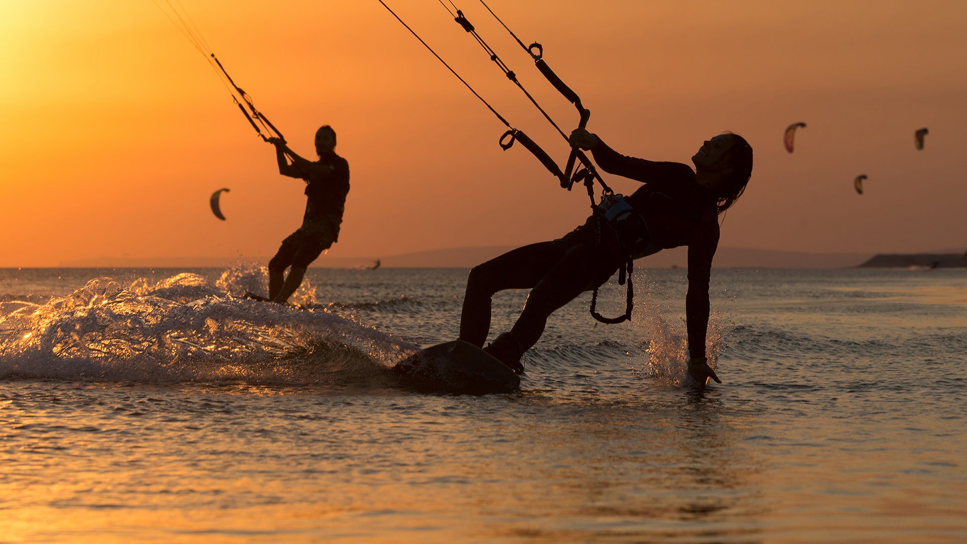 Can Pastilla Kitesurfing in Mallorca two kitesurfers in cheesy sundown with red light and more kitesurfers in the background