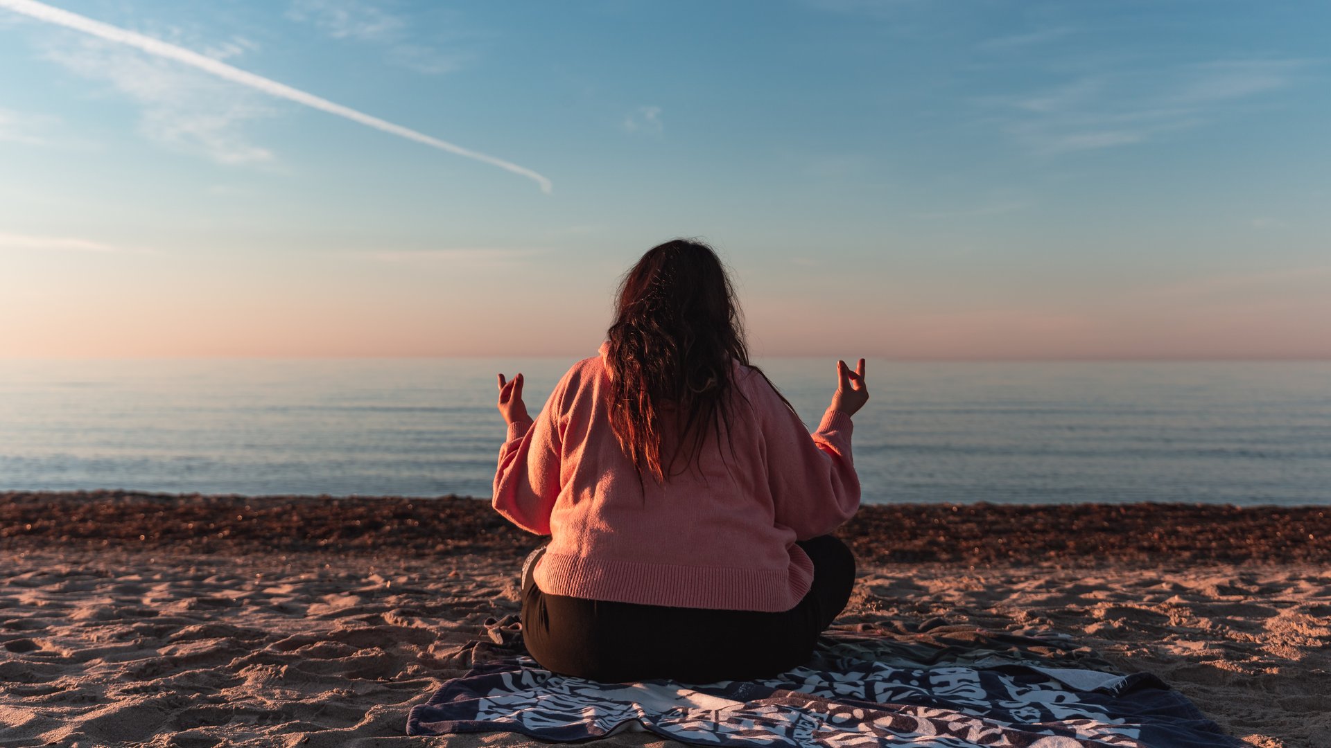 Beautiful lady with long red hair sitting at the beach in Poetto enjoying the sunset view
