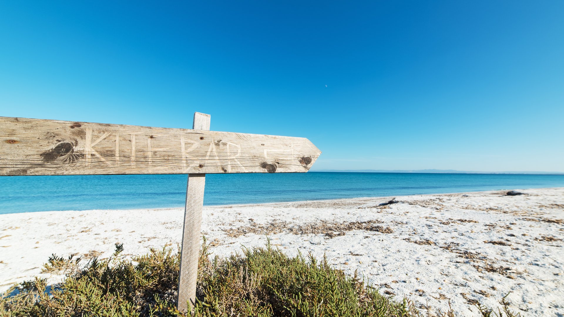 Le Saline Kitesurfing in Sardinia view from the white sandy beach with a signpost written “Kitebar” on it