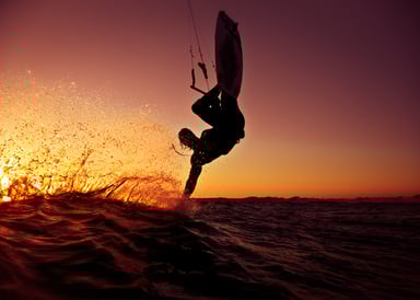 Agios Nikolaos Beach Kitesurfing in Greece kitesurfer making a trick touching the water surface with his hand flying over the water in a beautiful red sunset