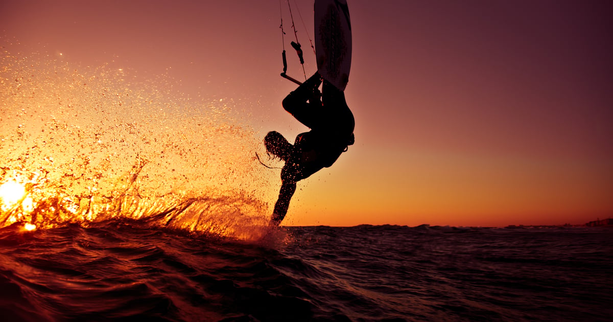 Agios Nikolaos Beach Kitesurfing in Greece kitesurfer making a trick touching the water surface with his hand flying over the water in a beautiful red sunset