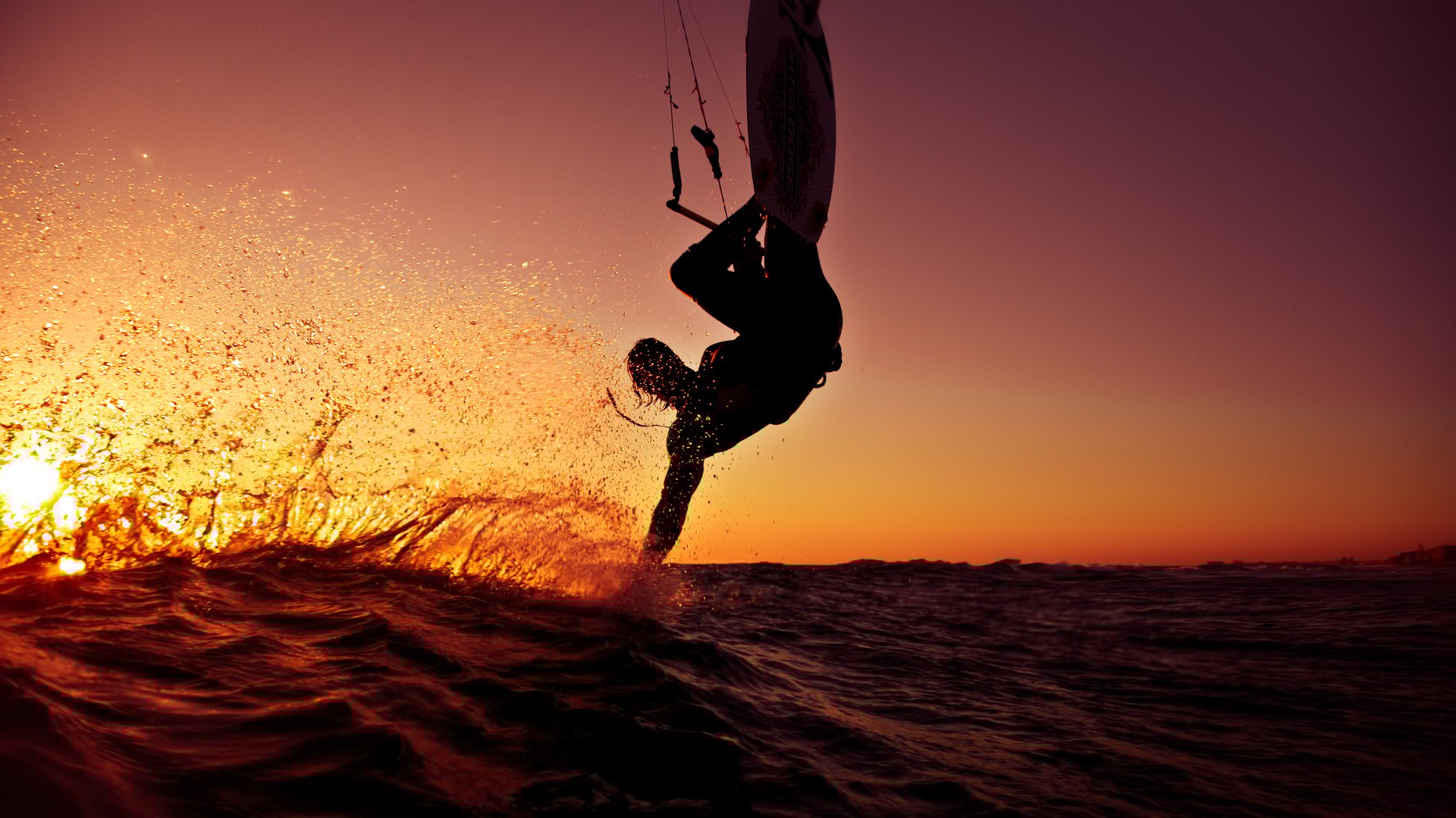 Agios Nikolaos Beach Kitesurfing in Greece kitesurfer making a trick touching the water surface with his hand flying over the water in a beautiful red sunset