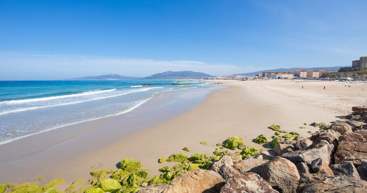 Balneario Kitesurfing in Tarifa with the shoreline, stones in front and a beautiful endless beach with sunny blue sky and mountains in the background
