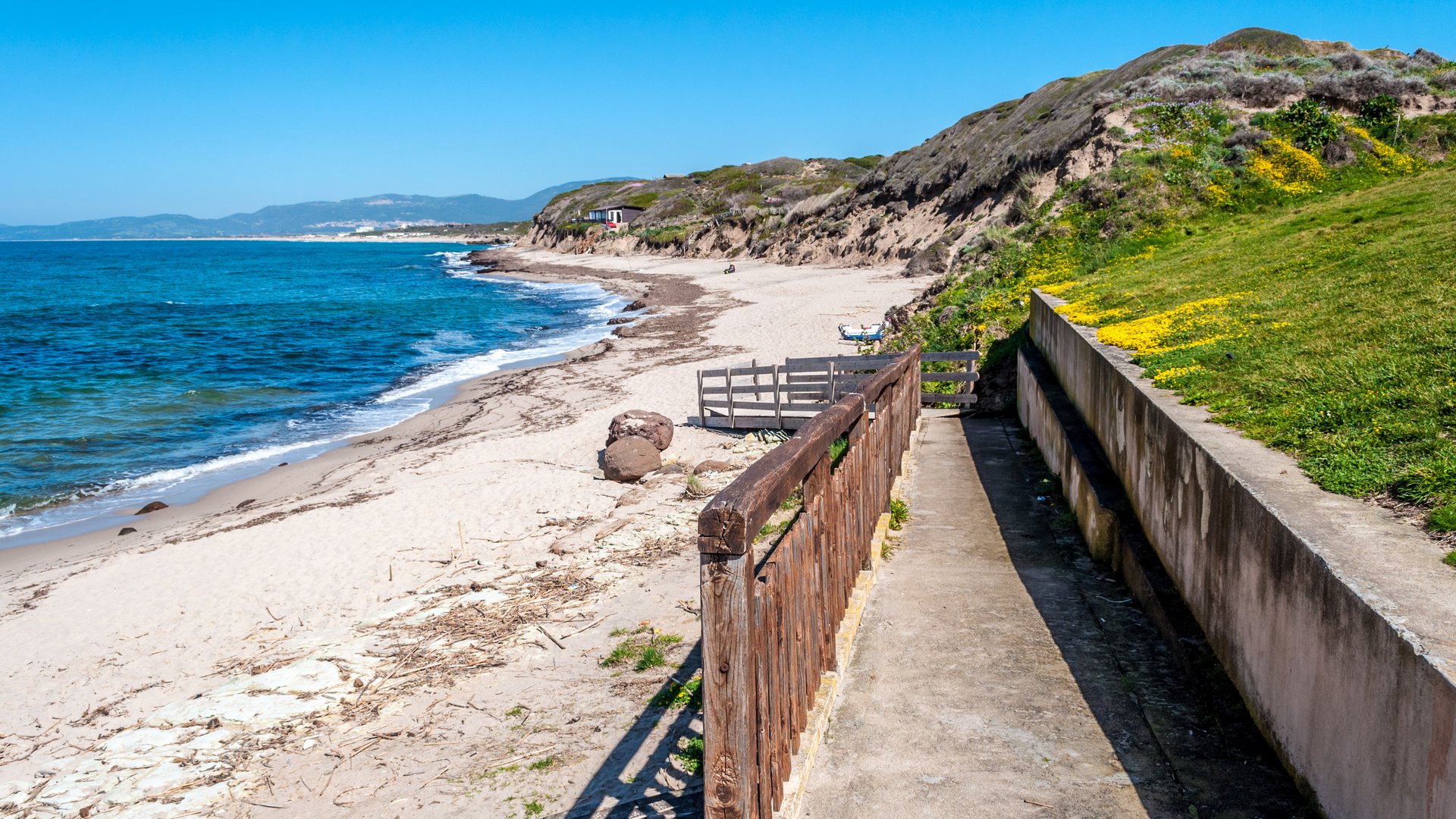 La Ciaccia Kitesurfing in Sardinia view along the sandy beach with green grass hills and the blue sea on the right side