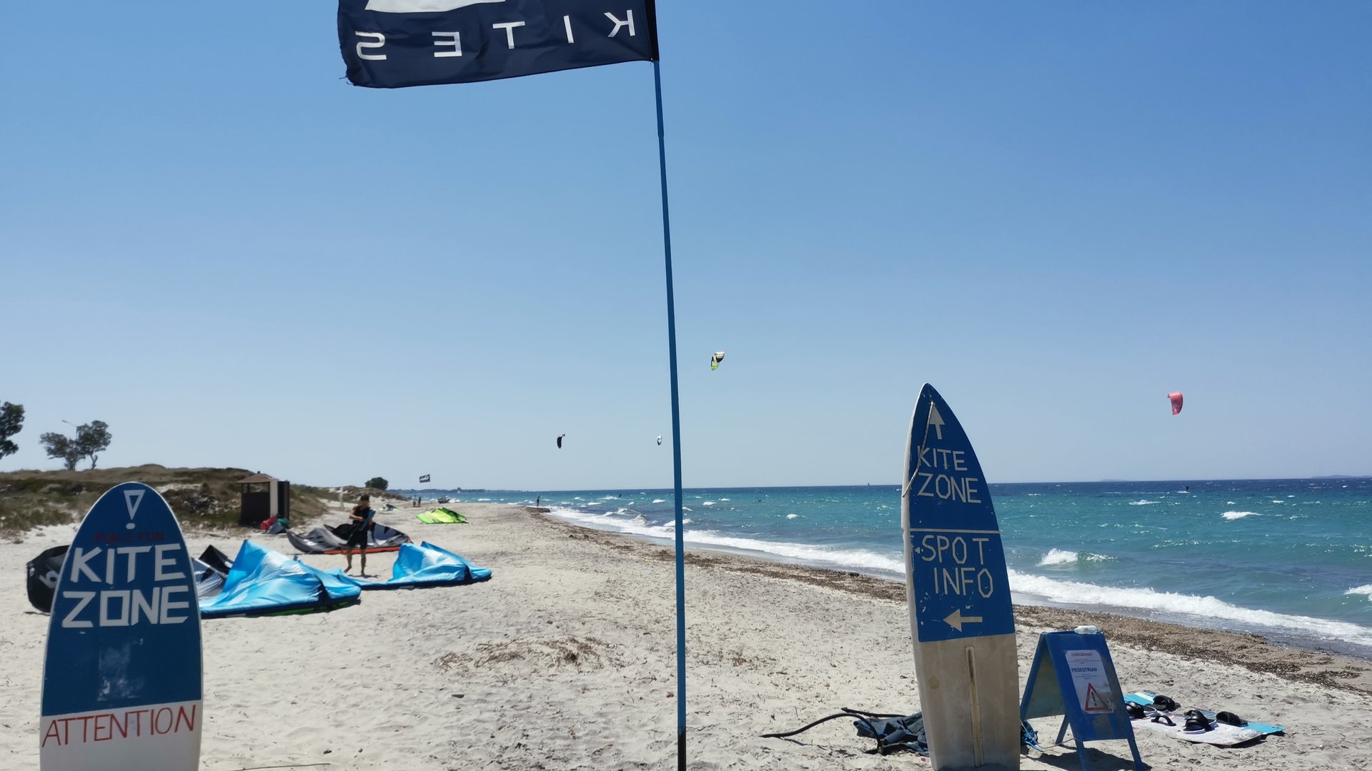 Marmari Beach Kiteboarding in Kos closeup at the beach with a black kite-flag and a few kitesurfers in the ocean on a sunny windy day