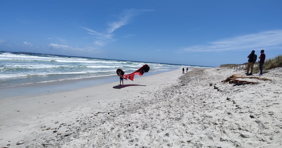 Gray Sand at Melkbos Kite Beach outside Cape Town. Small Waves crashin the ocean. Kitesurfer holding his kite. 