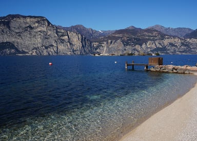 Brenzone Kiteboarding in Italy with cristal clear blue water at a small sandy beach and rocky steep mountains on the other side of Lake Garda