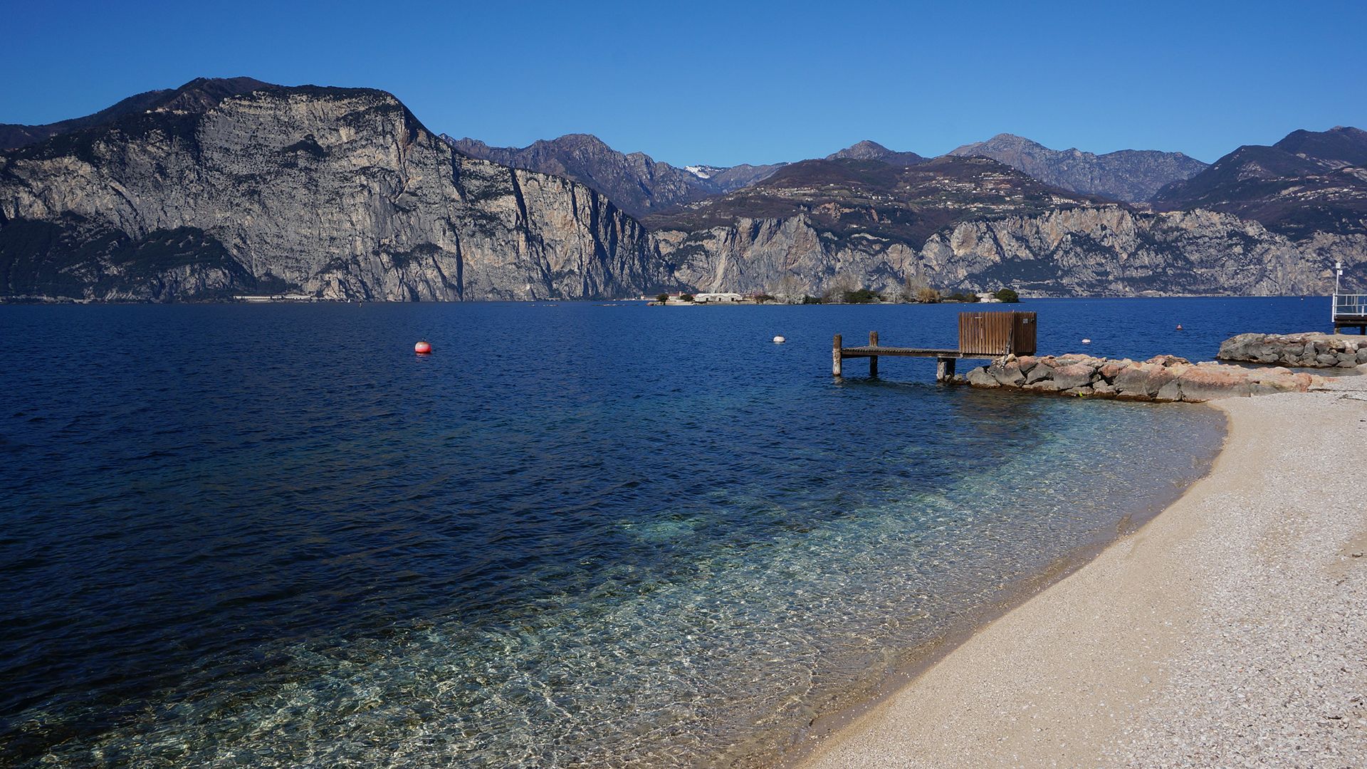 Brenzone Kiteboarding in Italy with cristal clear blue water at a small sandy beach and rocky steep mountains on the other side of Lake Garda