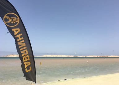 Dakhla Speed Spot Kitesurfing flag in front with Kitesurfers, sea and dunes in the background