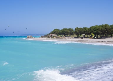 Kremaski Beach Kiteboarding in Rhodos Greec with bright blue water green trees and kiters in the background surfing on the water