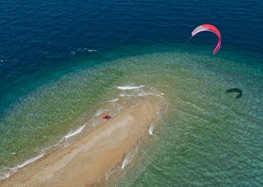 Cape Drepano Kitesurfing in Peleponnese in Greece beautiful aerial shot from above showing the edge ot the beach with turqoise water and a pink kite in the air