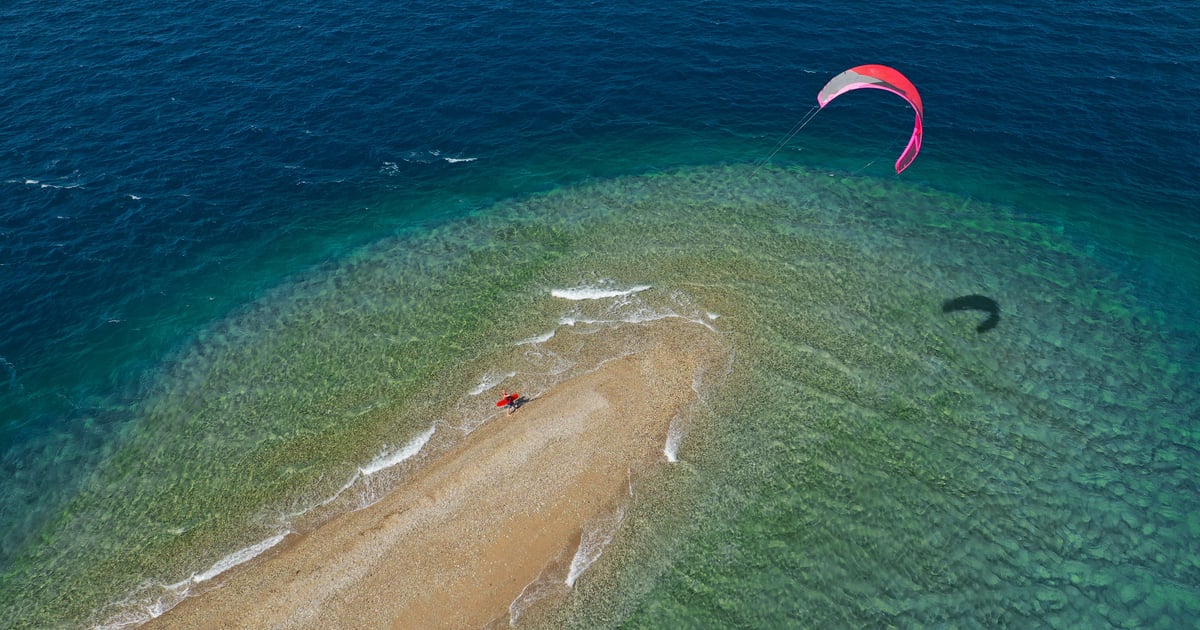 Cape Drepano Kitesurfing in Peleponnese in Greece beautiful aerial shot from above showing the edge ot the beach with turqoise water and a pink kite in the air