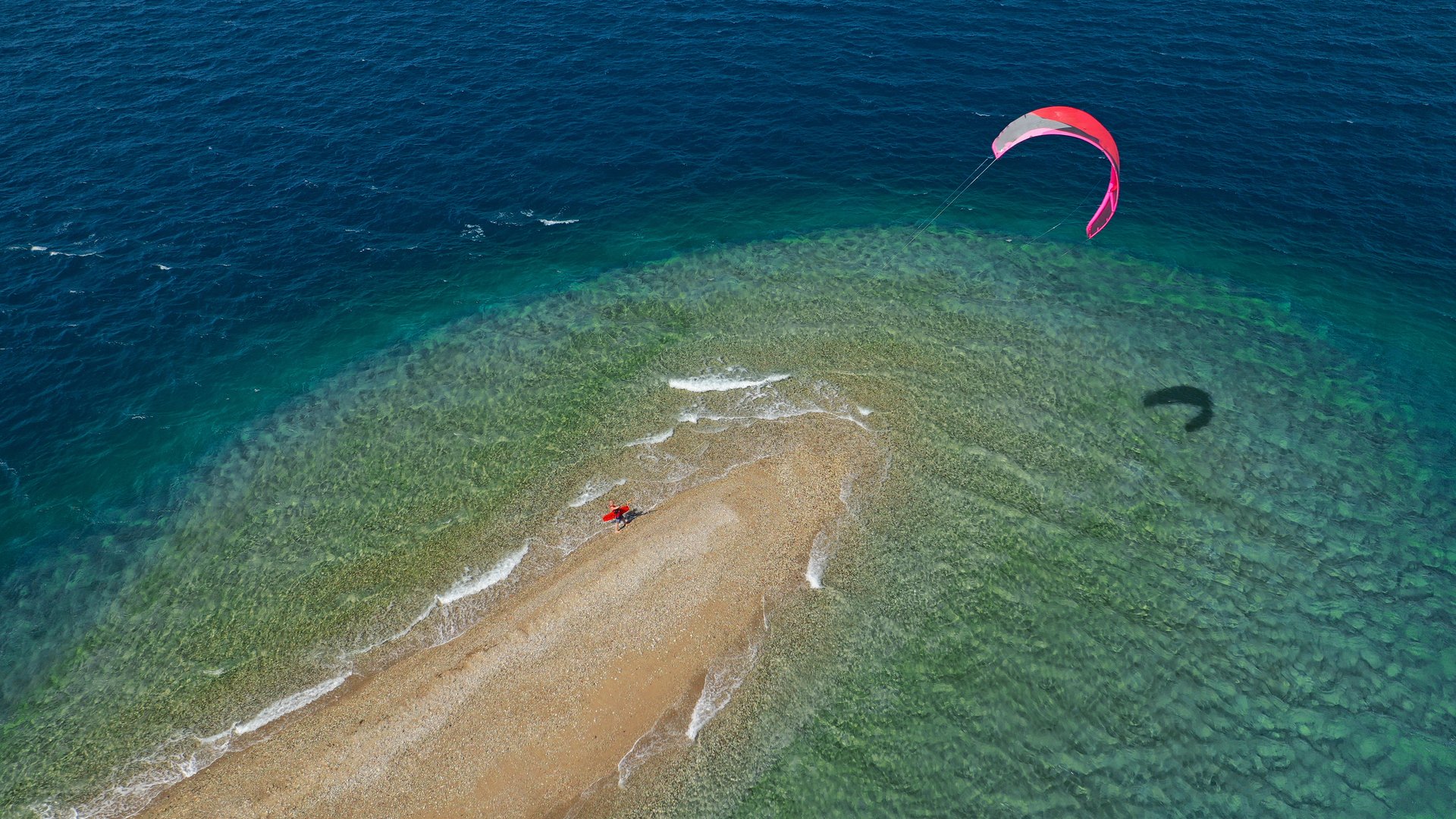 Cape Drepano Kitesurfing in Peleponnese in Greece beautiful aerial shot from above showing the edge ot the beach with turqoise water and a pink kite in the air